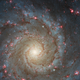 M74 in optical light—the galaxy's center is a pale yellow and it is peppered with pink splotches.